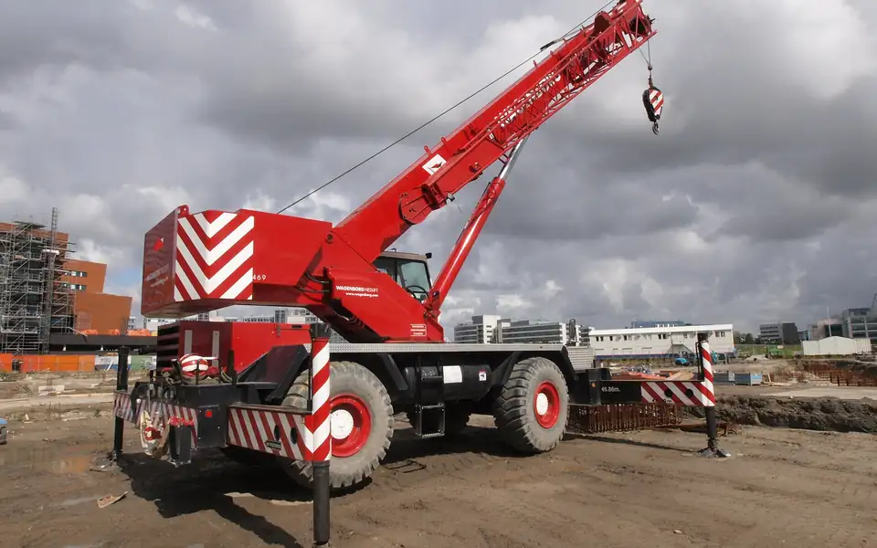 Red rough-terrain mobile crane with boom raised on a construction site